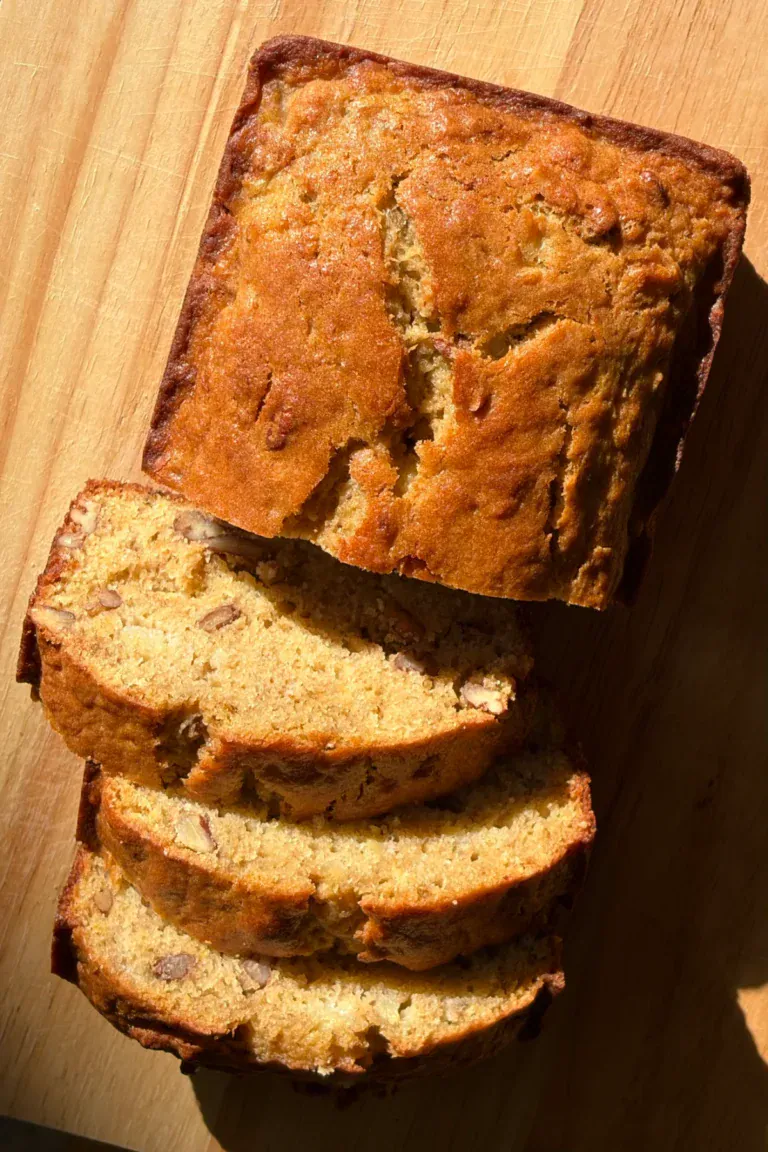 banana bread loaf that has been sliced, sitting on a wood cutting board